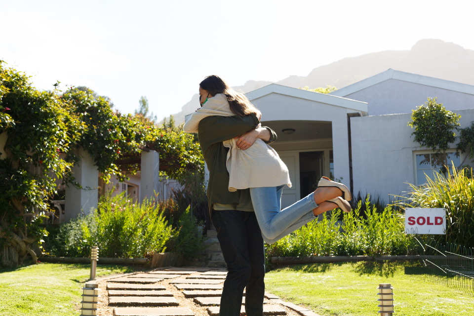 couple embraces in front of house with sold sign