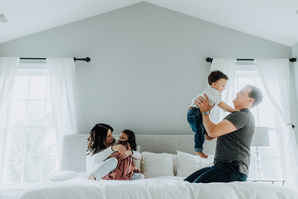 family playing on bed in bright, white space